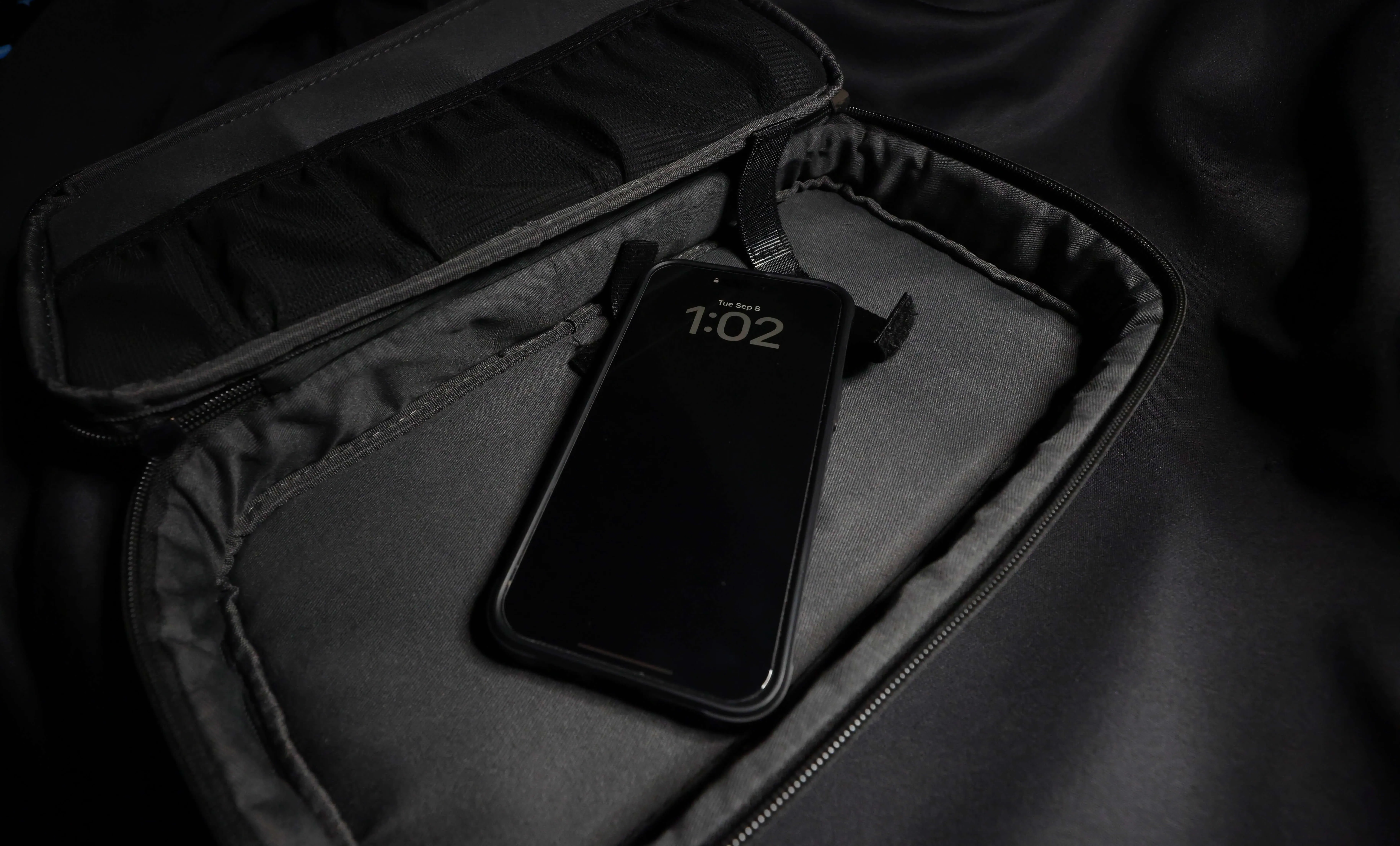 A smartphone showing 1:02 on a Tuesday, September 8th lock screen, resting inside the padded, open compartment of a dark gimbal travel case.