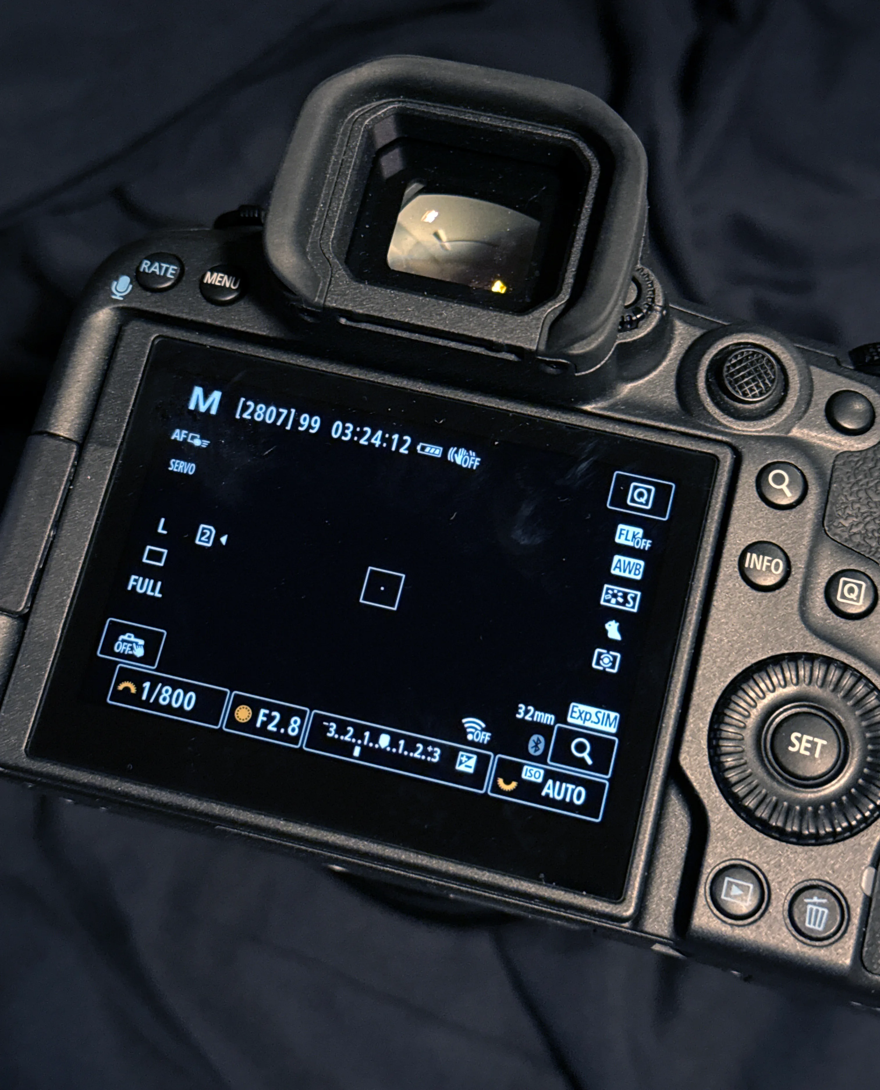 Canon mirrorless camera's rear LCD screen showing Manual mode settings, 1/800 shutter speed, F2.8 aperture, and Auto ISO, viewed from behind through the eyecup.