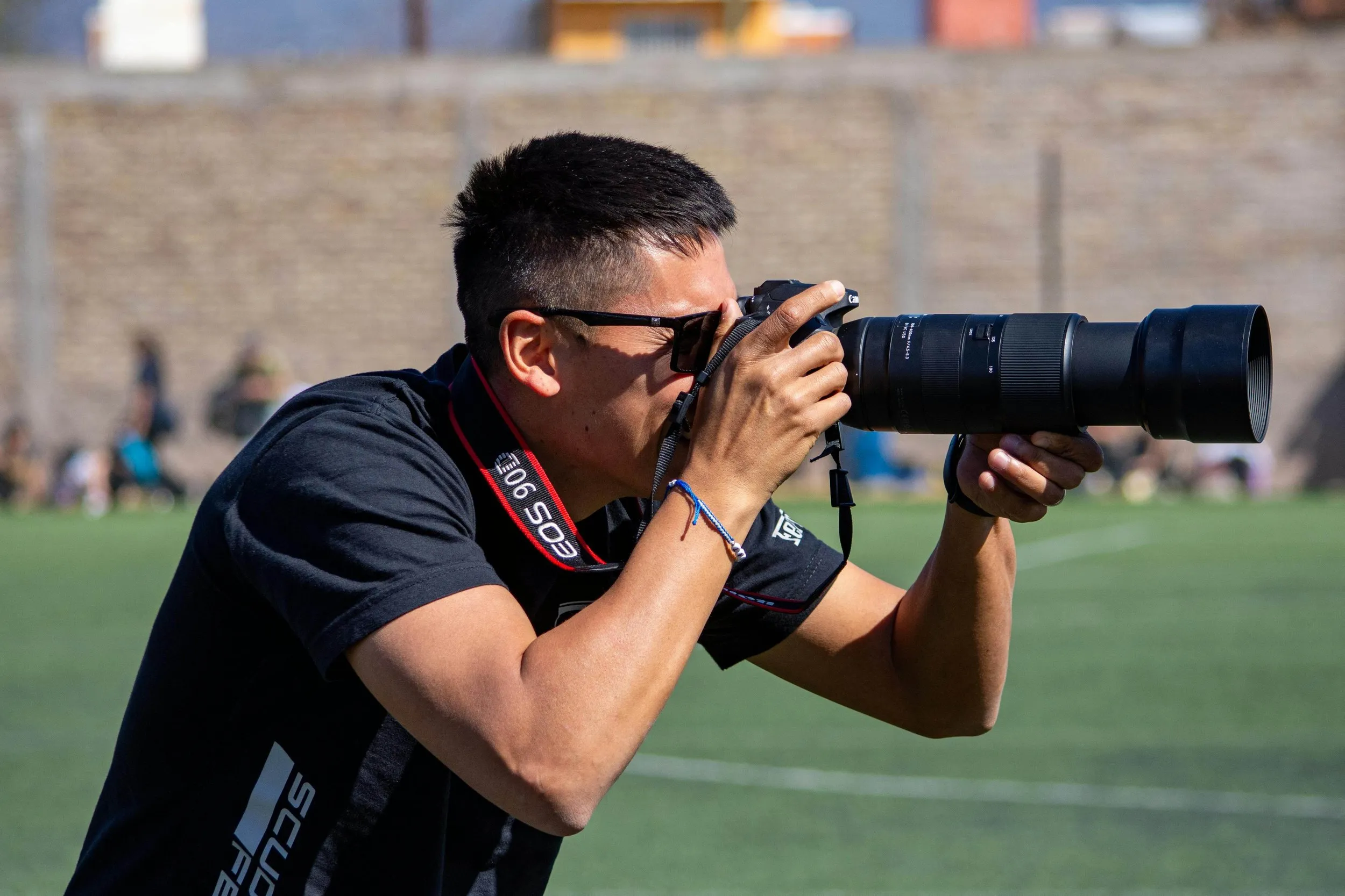 A photographer on the sidelines of a soccer game, camera raised, shooting the action.