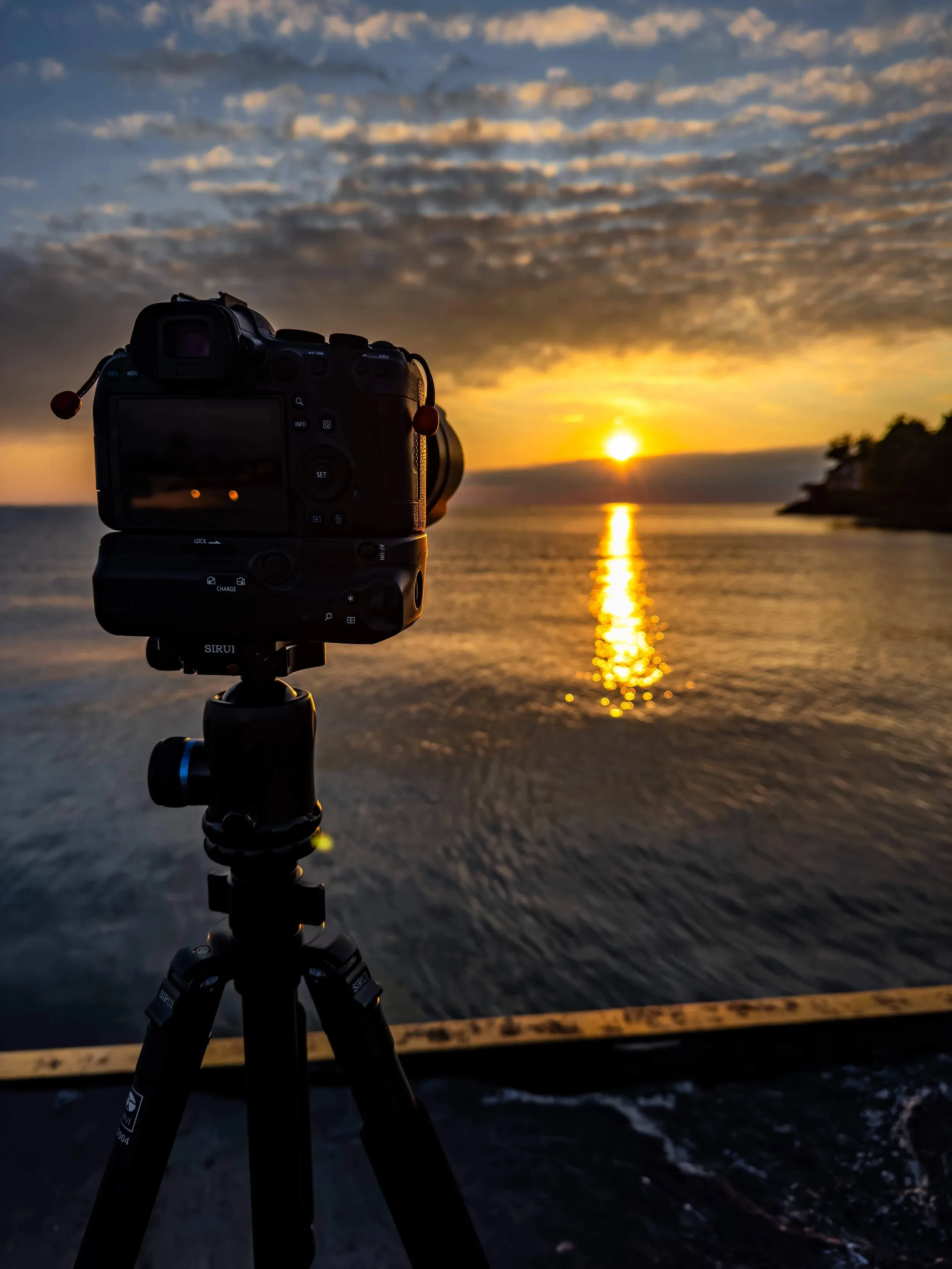A camera on a tripod silhouetted against a golden sunset over water, the instrument ready for the story.