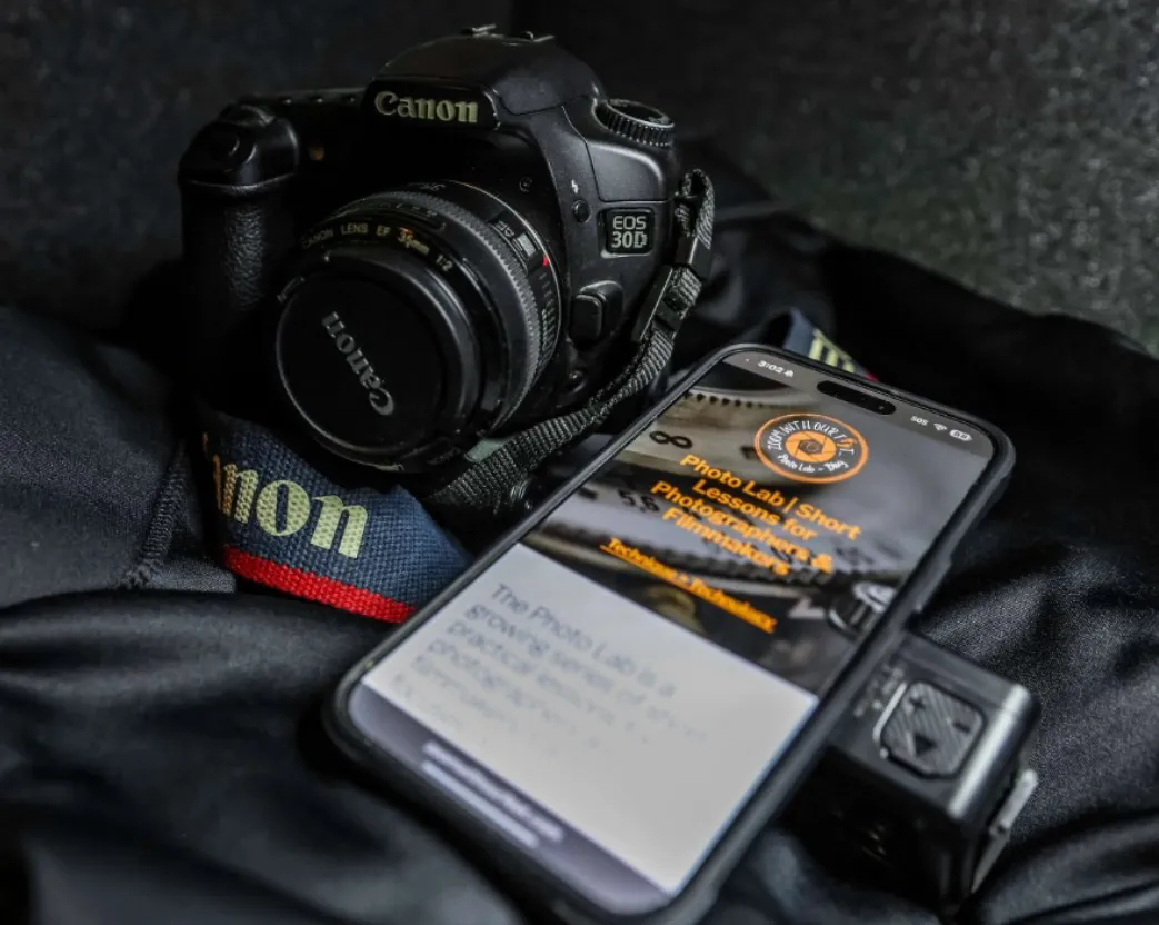 An old Canon EOS 30D DSLR camera next to a smartphone displaying the Zoom With Our Feet Photo Lab website.